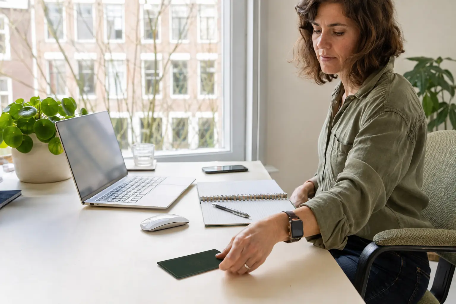 Een hand legt een tarotkaart naast laptop, telefoon en notitieboek op een moderne werkplek